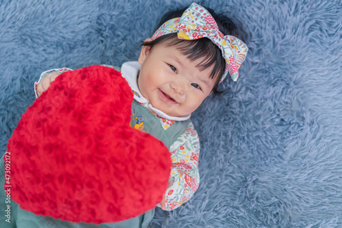 Asian baby valentine with red heart smiling and laying on carpet. Cute 6 months baby smling, laughing and laying use as concept of valentine, love, baby or kid department in hospital.