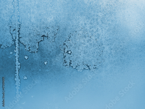 Frozen and misted window glass. Abstract winter background or wallpaper. Ice crystals and water droplets. Blue tinted natural backdrop. Misty or translucent surface