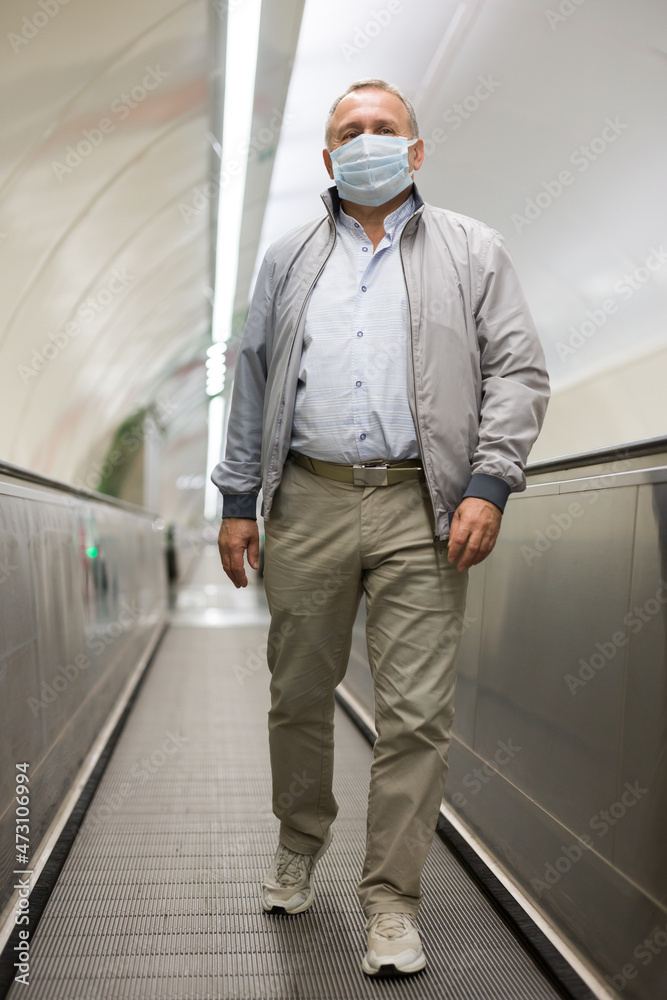 Elderly man in protective mask walks along a travelator in underground metro