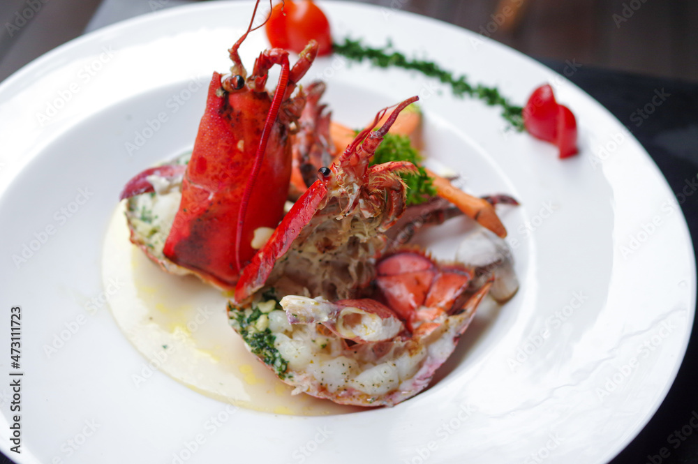 steamed american lobster with basil pesto and cherry tomato on round white plate top view