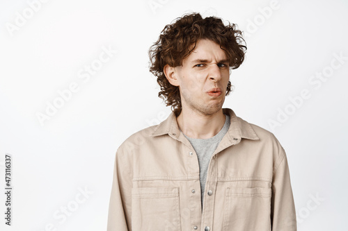 Close up of funny guy express aversion and dislike, grimacing from smth disgusting, standing over white background