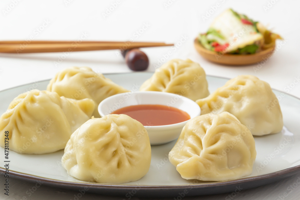 Boiled dumplings, manti or wontons with minced meat in a plate with sauce on a white table along with chopsticks and a bowl of salad. Homemade food. View from above