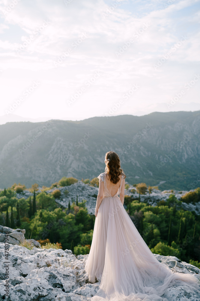 Bride stands on a rocky mountain and looks out over the bay