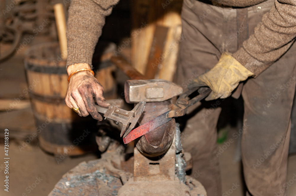 Detail shot of hammer forging hot iron at anvil