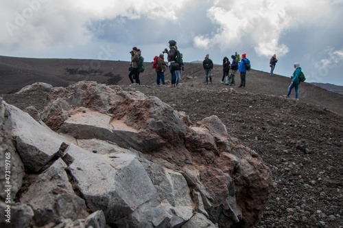 Primo piano roccia con escursionisti sullo sfondo Vulcano Etna photo