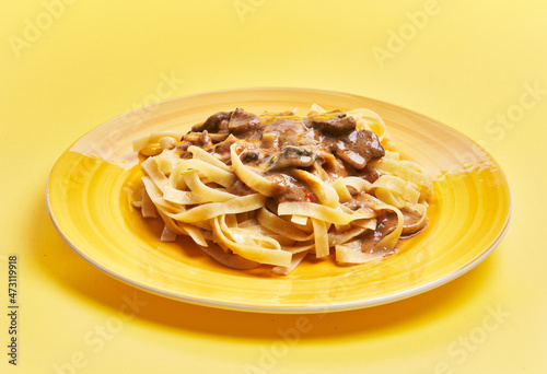  Plate of italian tagliatelle pasta with mushroom sauce over yellow background