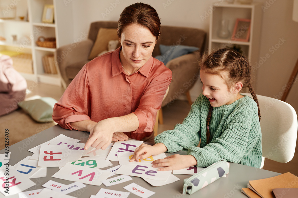 Little girl learning english together with the teacher at home, they sitting at the table and reading letters Little girl learning english together with the teacher at home, they sitting at the table and reading letters