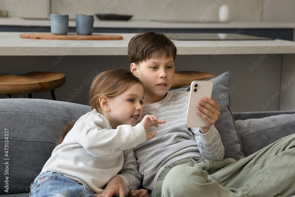 Addicted to modern tech happy small adorable children siblings using cellphone software applications, playing entertaining mobile games, watching funny videos, spending time online, sitting on couch. Addicted to modern tech happy small adorable children siblings using cellphone software applications, playing entertaining mobile games, watching funny videos, spending time online, sitting on couch.