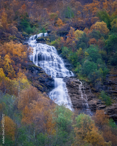 A wild Norwegian waterfall in the fall forest near the village of Geiranger