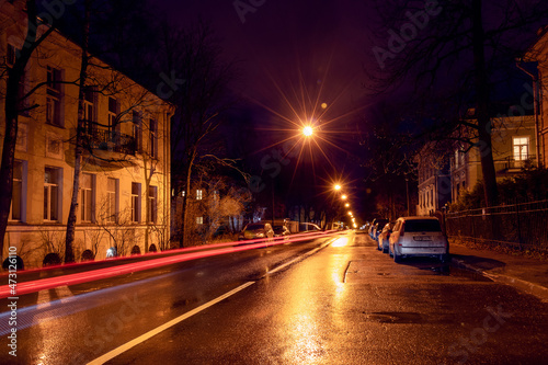 Night city street with lights of passing car, trees and street lamps © Maria