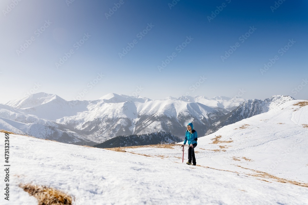 Woman hiker tourist climbing with pickax in snowy winter mountains. Polish Tatra mountains