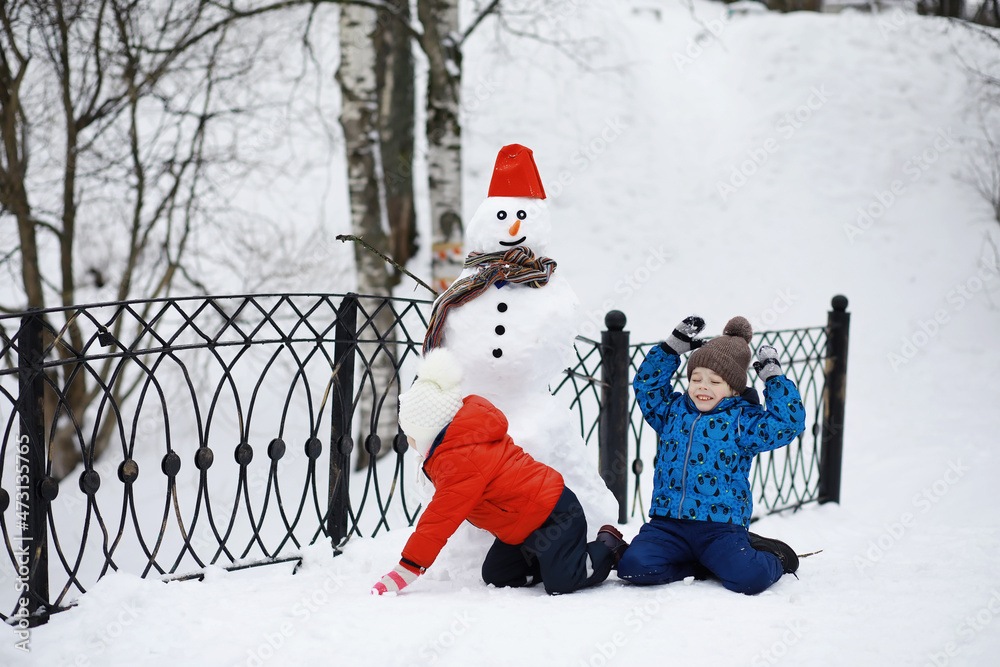 Children in the park in winter. Kids play with snow on the playground. They sculpt snowmen and slide down the hills.