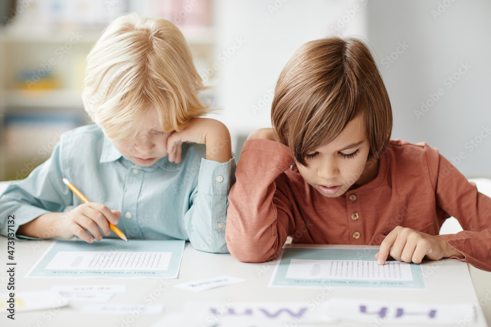 School children making notes on paper while sitting at the table during lesson School children making notes on paper while sitting at the table during lesson