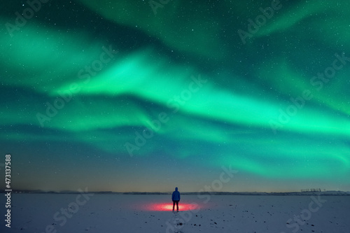Tourist with red flashlight on snowy field against the backdrop of incredible starry sky with Aurora borealis. Amazing night landscape. Northern lights in winter field