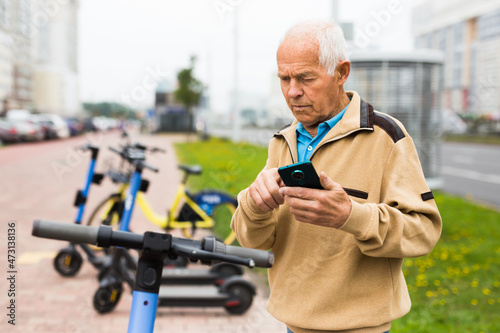 Old man using smartphone to activate e-scooter