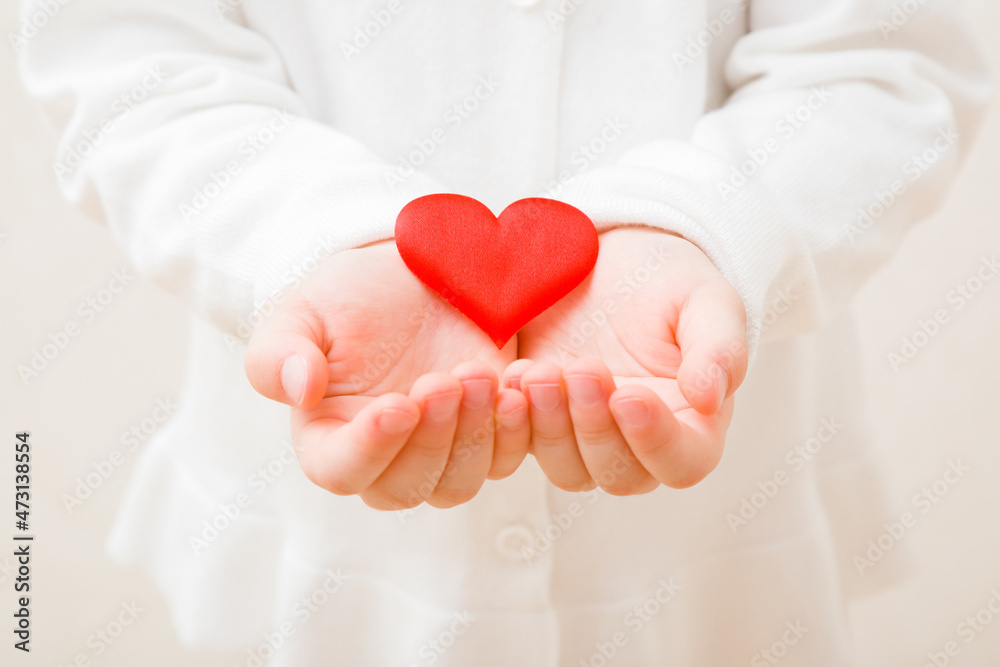 Baby girl hands holding and showing bright red heart shape. Toddler in white clothes. Closeup. Front view. Love concept. Baby girl hands holding and showing bright red heart shape. Toddler in white clothes. Closeup. Front view. Love concept.
