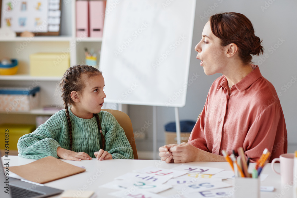 English teacher teaching to pronunciate and reading the words the little girl while they sitting at the table with cards English teacher teaching to pronunciate and reading the words the little girl while they sitting at the table with cards