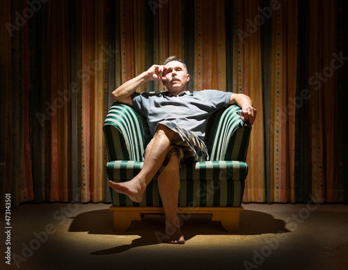 Elderly man is sitting in a dark room in a vintage armchair under the light of a lamp photo