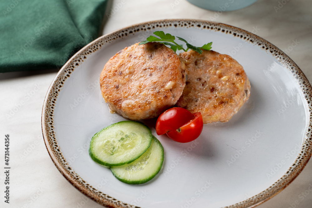 Two golden roasted salmon cutlets with two slices of cucumber and cherry tomatoes, top view with copy space