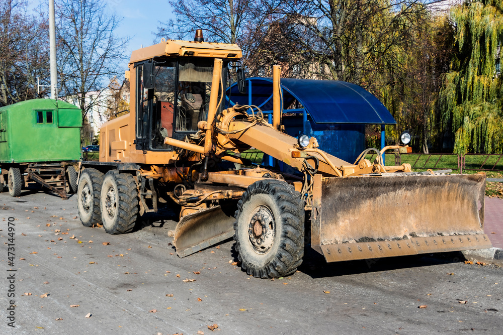 A grader performing road works in the center of a modern city. Road works in the fall.