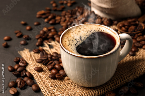 Cup of aromatic hot coffee and beans on black table, closeup