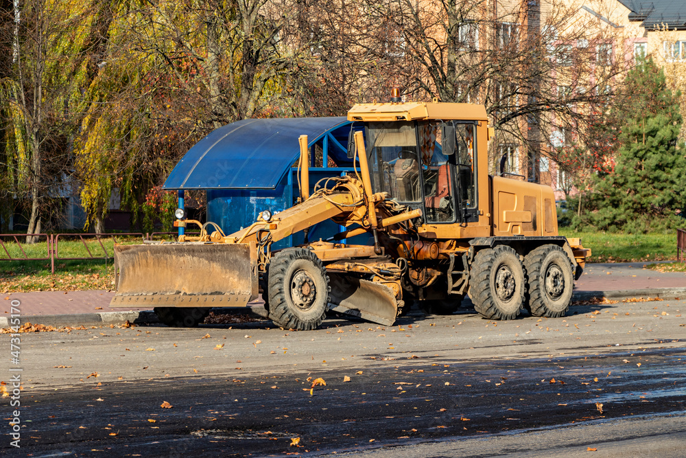 A grader performing road works in the center of a modern city. Road works in the fall. A grader performing road works in the center of a modern city. Road works in the fall.