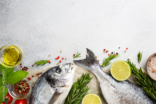 Fresh ready to cook raw bream fish dorado with ingredients and seasonings like rosemary, salt, pepper, lime and olive oil, top view photo