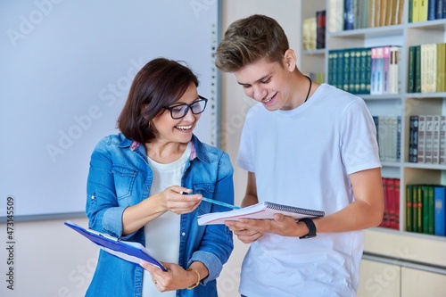 College student guy teenager meeting discussing with teacher mentor in classroom