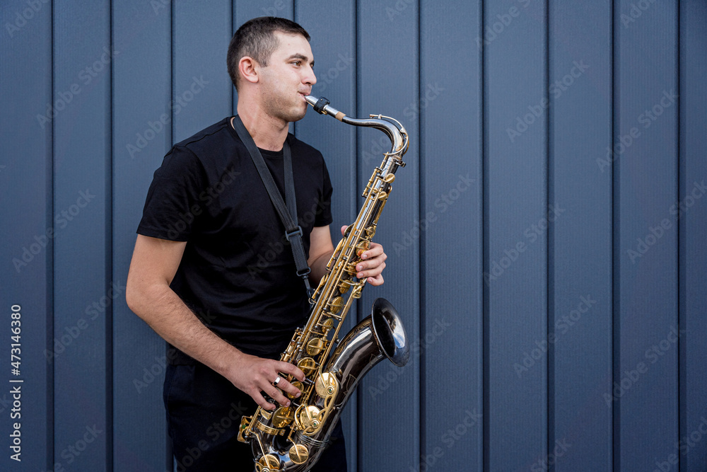 Naklejka premium Young street musician playing saxophone near the big blue wall