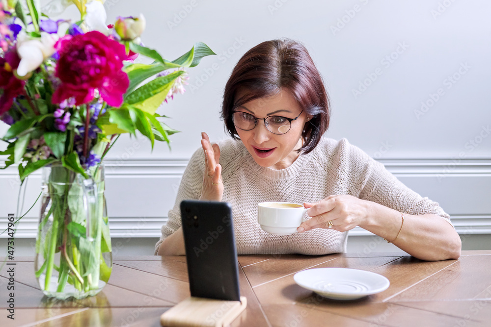 Middle-aged woman sitting at home using smartphone for video call Middle-aged woman sitting at home using smartphone for video call