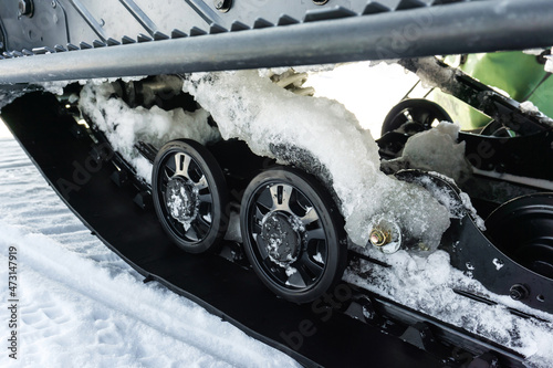 Snowmobile wheels and tracks are covered with ice. Fragment of a vehicle for moving on snow. Close-up