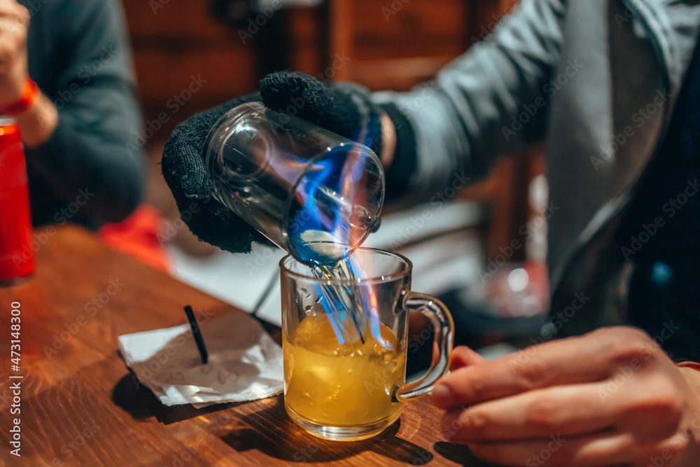 A man makes cocktails at home. Burning absinthe in a glass mug. The fire pours into the mug.