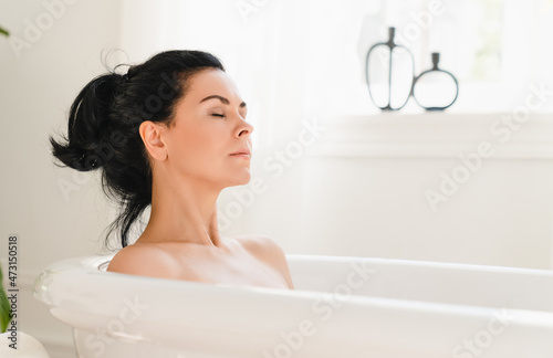 Caucasian middle-aged woman with closed eyes enjoying hot warm bath water in spa bathroom, relaxing after work day at home