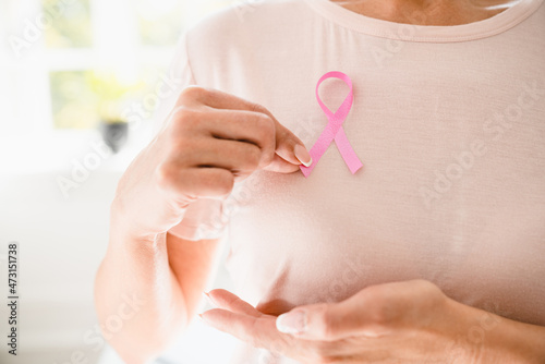 Caucasian woman in pink t-shirt doing palpation with pink ribbon on her breast to support world breast cancer day. Fighting against tumors, recovery from oncology photo