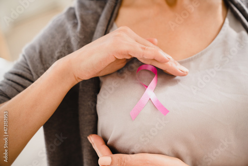 Caucasian woman doing palpation with pink ribbon on her breast to support world breast cancer day. Fighting against tumors, recovery from oncology photo
