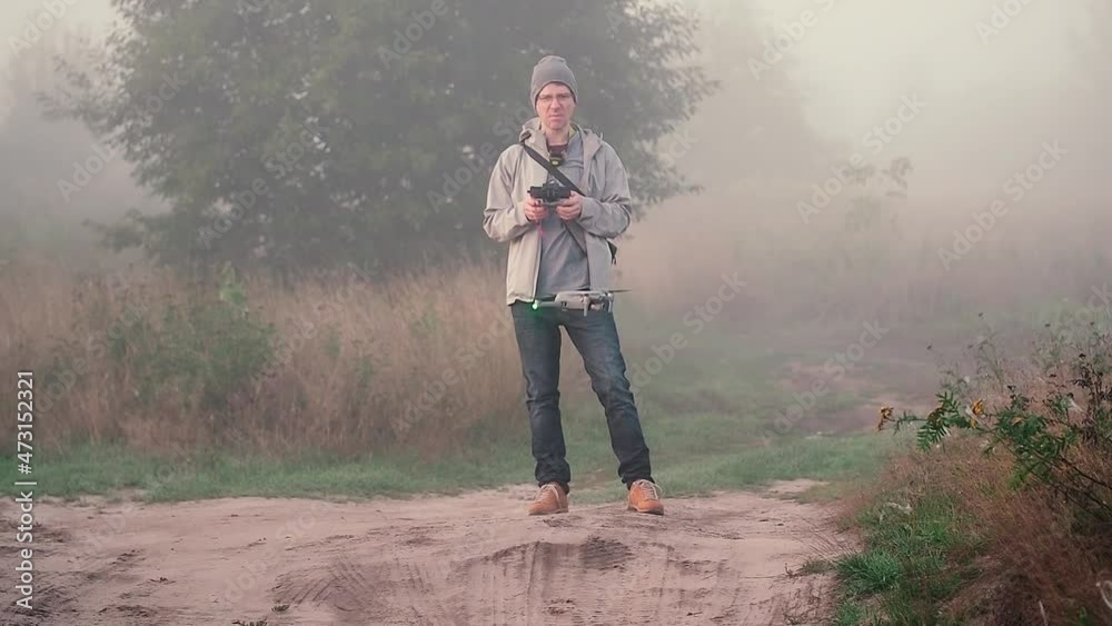 A man with a remote control instructs his drone to take off. The drone takes off and hovers at the human level, waiting for the upcoming flight mode setting. A sandy country road, thick fog A man with a remote control instructs his drone to take off. The drone takes off and hovers at the human level, waiting for the upcoming flight mode setting. A sandy country road, thick fog