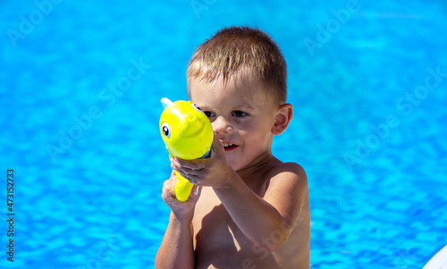 Happy child in the pool playing with a water gun.