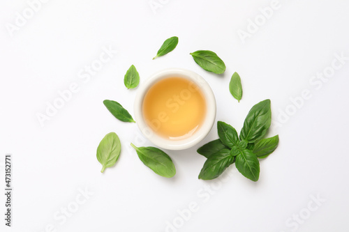 Essential basil oil and fresh leaves on white background, flat lay