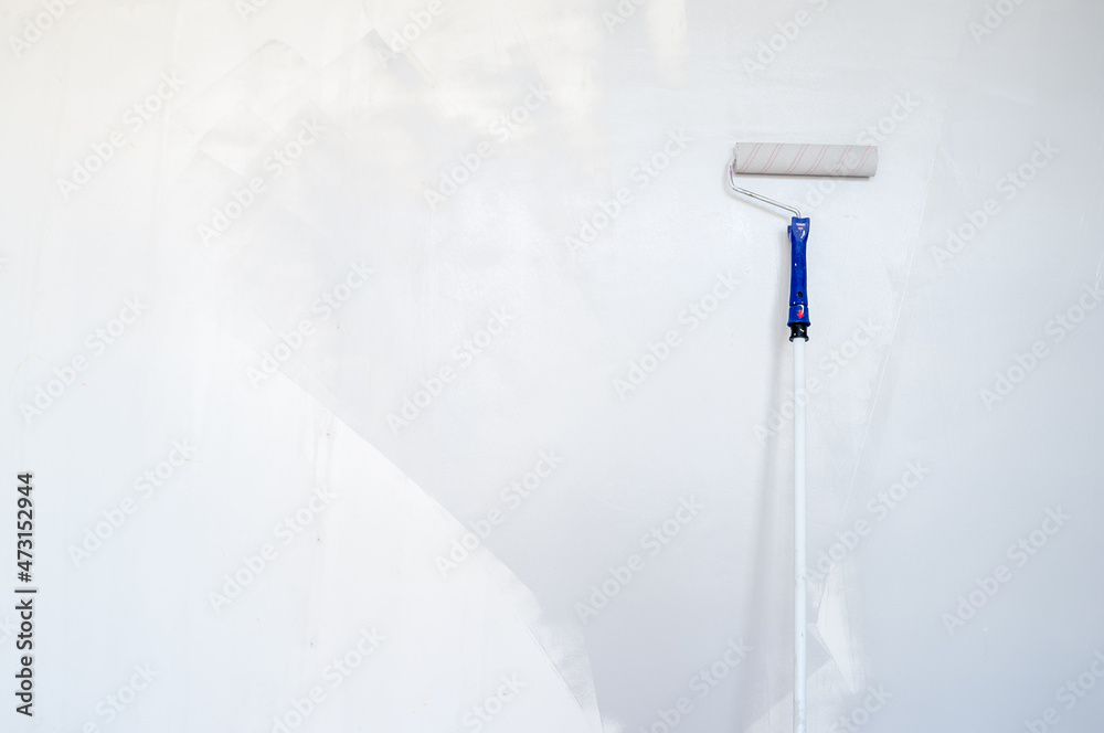 Sponge roller on a wooden stick repaints the wall gray. Home renovation. Copy space. 