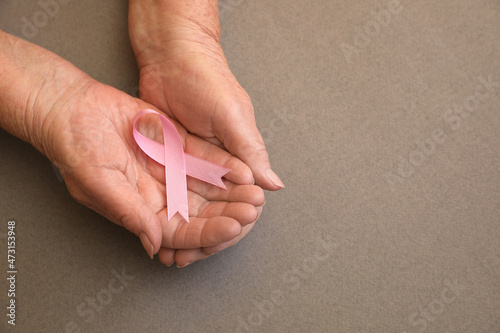 Senior woman holding pink ribbon on grey background, top view with space for text. Breast cancer awareness