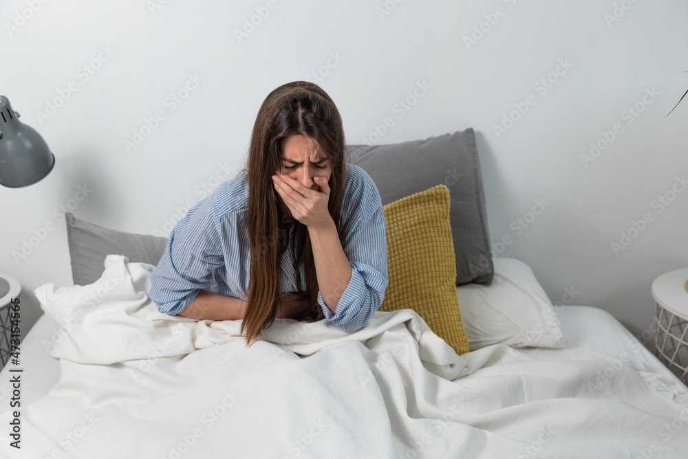 Young woman lying in the bed feeling sick holding her painful stomach