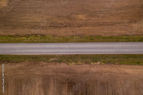 Drone photography of road through plowed field during summer day.