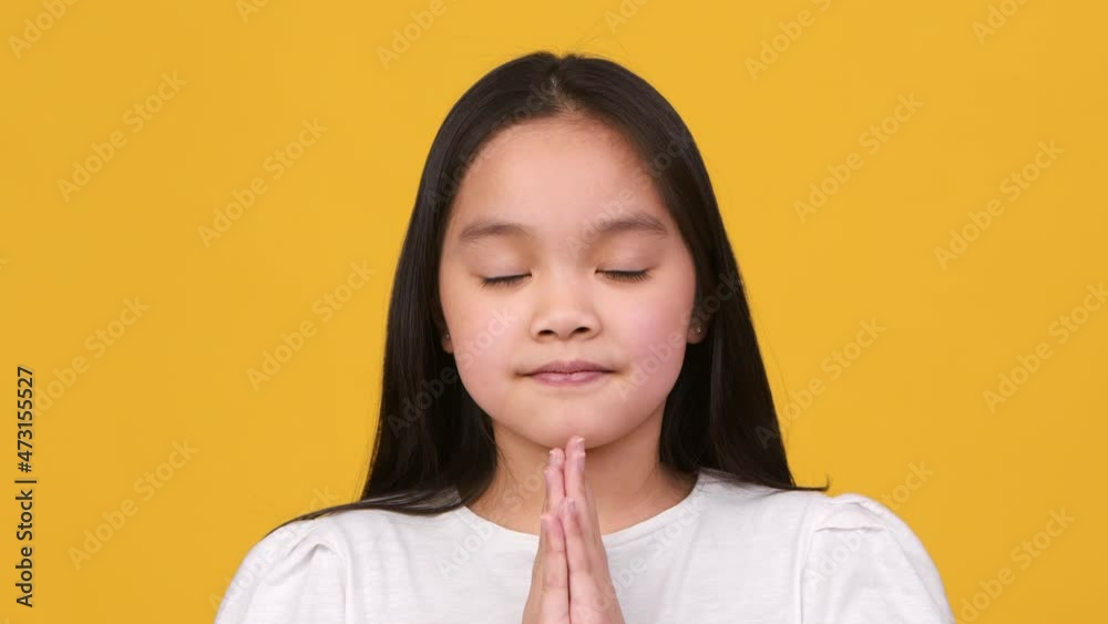 Sincere kids faith. Cute little asian girl praying to God, making prayer gesture with closed eyes and looking at camera Sincere kids faith. Cute little asian girl praying to God, making prayer gesture with closed eyes and looking at camera