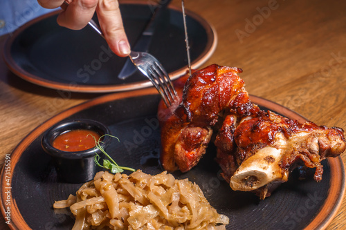 A man cuts a pork knuckle with a knife and fork with stewed cabbage on a plate.