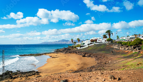 View of Playa El Barranquillo beach in Puerto del Carmen, Lanzarote. Sandy beach with turquoise ocean waves, white houses and mountains, Canary Islands, Spain photo