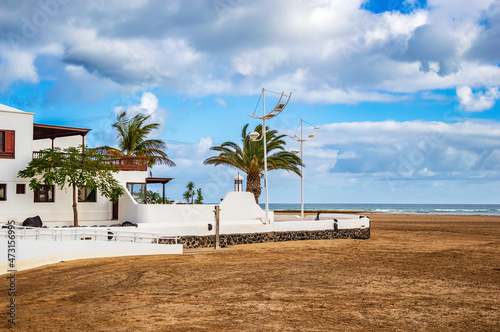 Fototapeta Naklejka Na Ścianę i Meble -  Typical white houses on beach of Playa Honda on Lanzarote island, Spain. Vacation home near sea with palm trees and sandy beach under blue sky on Canary Islands