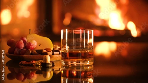 One glass with whiskey and plate with chocolate,
 grapes, pear on the fireplace background.
