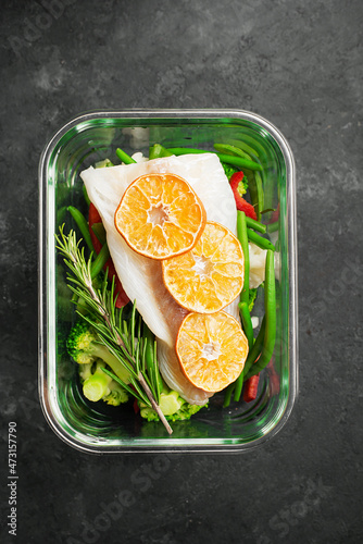 White cod fish fillet box. Fresh vegetables with a slice of cod in a glass container. Top view.