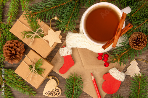 Craft gift boxes, craft envelope and wooden toys, green Christmas tree branches and white mug of tea on dark wooden background top view
