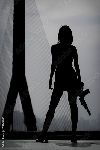 Silhouette of a woman holding a gun with a cloudy sky in the background.